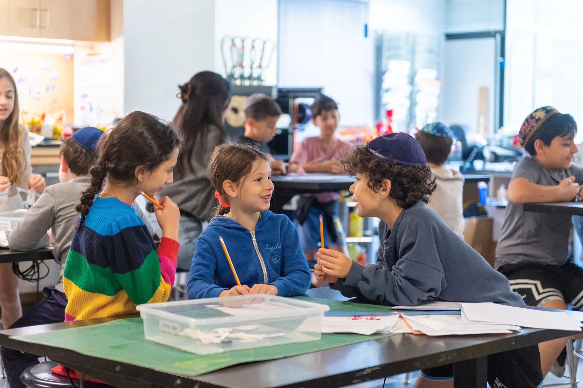 Two girls and a boy talking in a classroom.